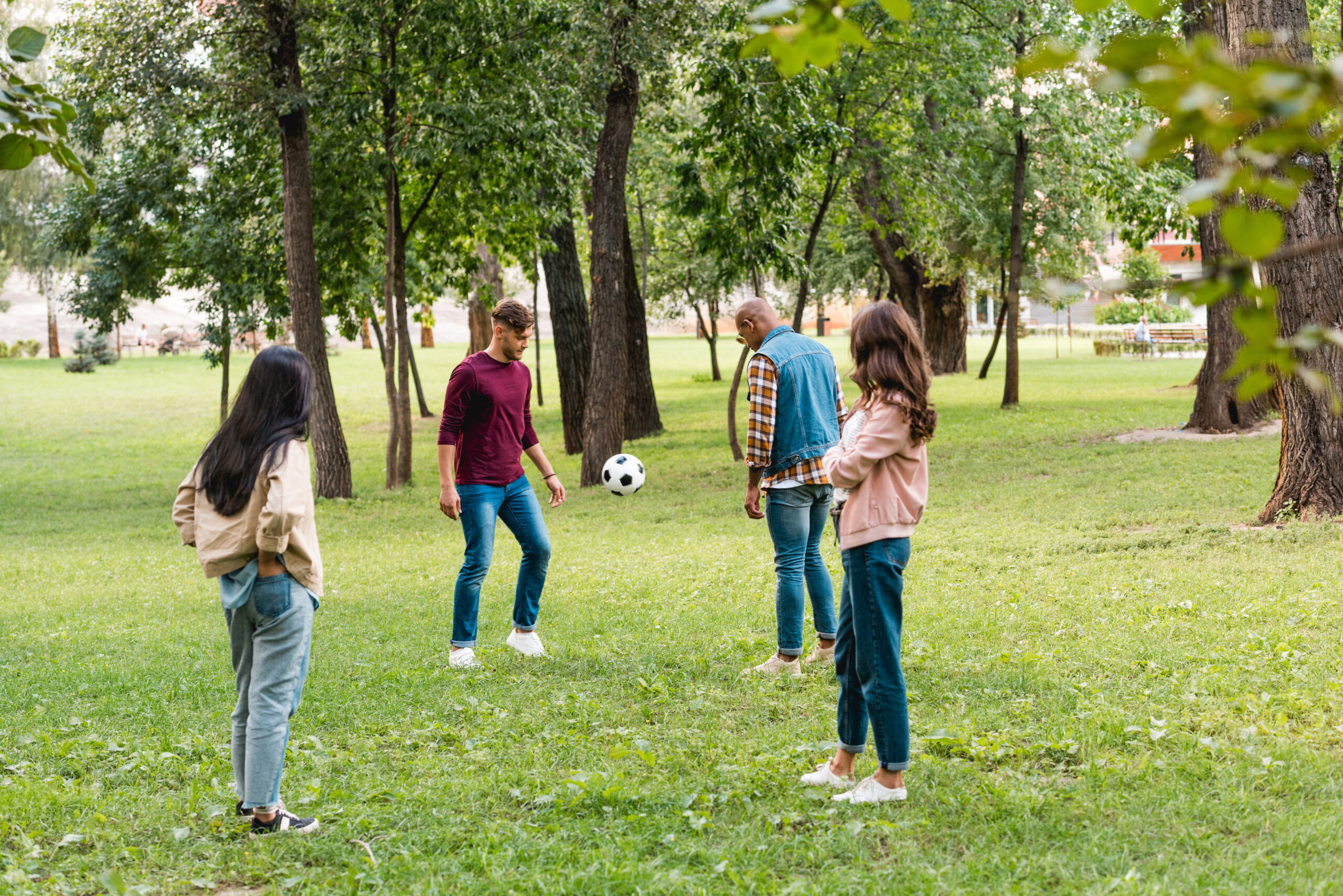 A group of friends stand in a park, kicking around a soccer ball.