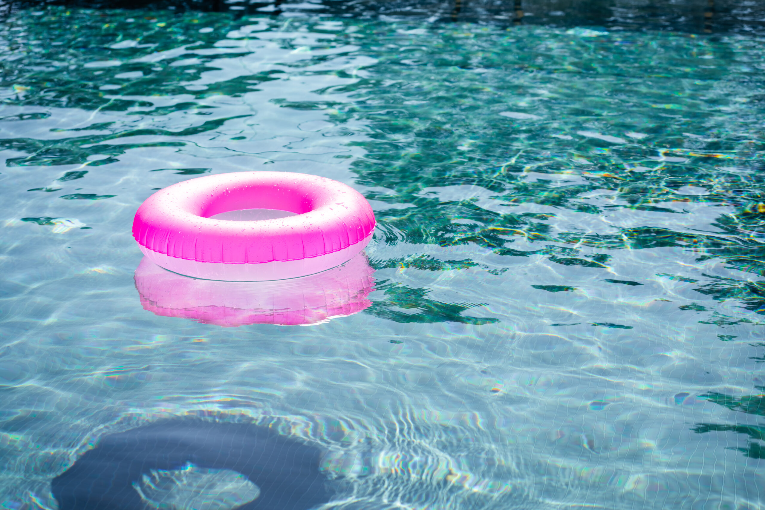 An empty pink inner tube is floating in a clear, blue pool.